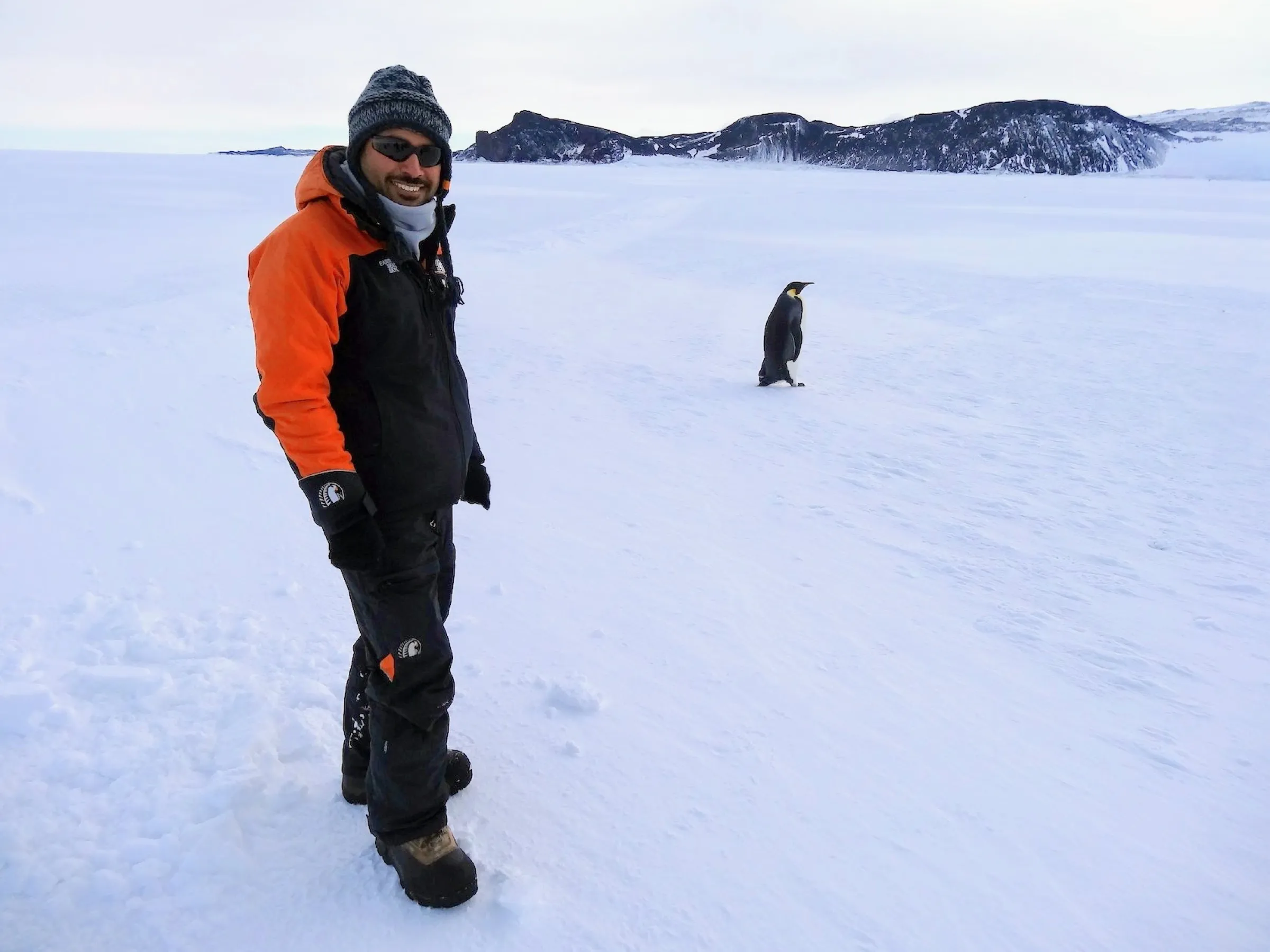Iman in polar gear on the Antarctic ice, with an emperor penguin standing a few metres away.